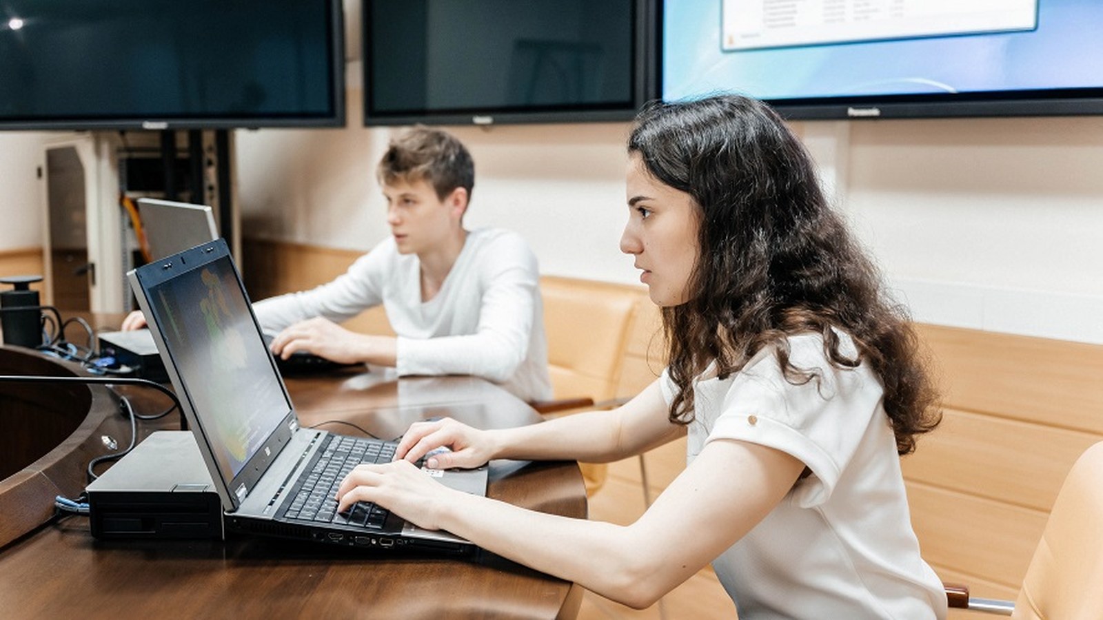 Two colleagues using laptops together in a conference room